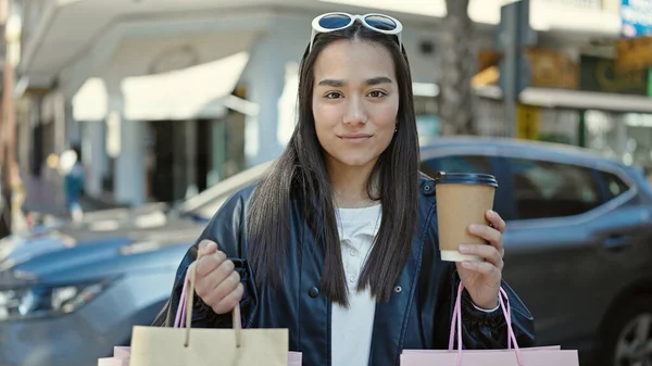 若い美しいヒスパニックの女性は自信を持ってショッピングバッグやコーヒーショップテラスでコーヒーを保持笑みを浮かべて — ストック写真