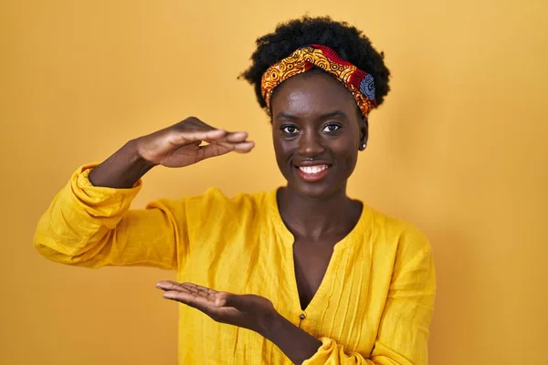 非洲年轻女子头戴非洲头巾 手拿着大号和大号的头巾 象征着什么 微笑着看着摄像机 计量概念 — 图库照片