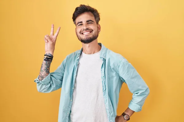 Junger Hispanischer Mann Mit Tätowierungen Vor Gelbem Hintergrund Der Lächelnd — Stockfoto