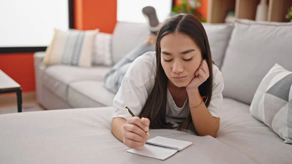 stock image Young beautiful hispanic woman writing on notebook lying on sofa at home