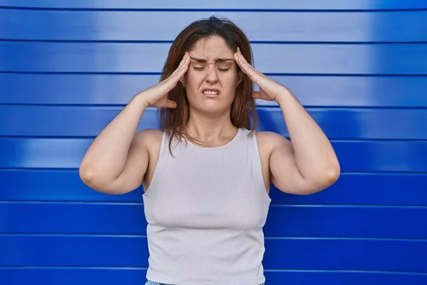 ブルネットの女性の頭の上に手で青の背景に立って 頭痛の種ので ストレス 片頭痛 — ストック写真