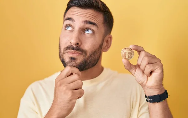 Handsome Hispanic Man Holding Tether Cryptocurrency Coin Serious Face Thinking — Stock Photo, Image