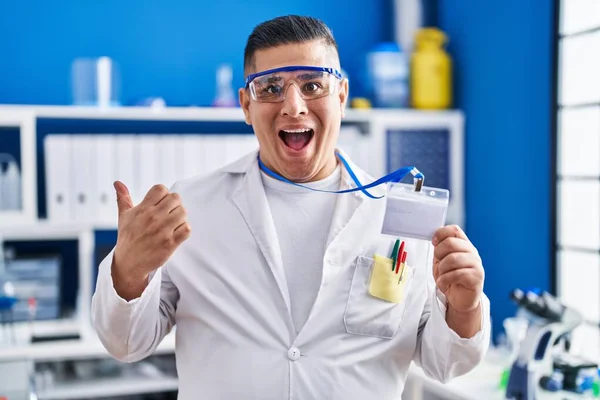 Hispanic Young Man Working Scientist Laboratory Holding Card Pointing Thumb — Stock Photo, Image