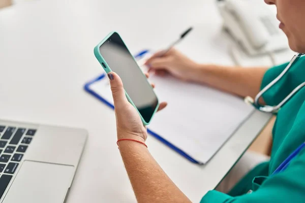 Dokter Muda Hispanik Menggunakan Smartphone Menulis Pada Dokumen Klinik — Stok Foto