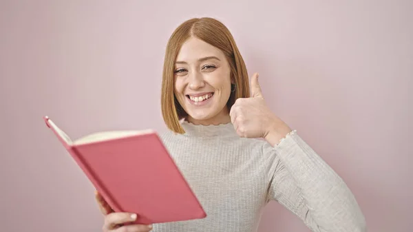 年轻的金发女人微笑着 自信地读书 在孤立的粉色背景下做着大拇指向上的手势 — 图库照片
