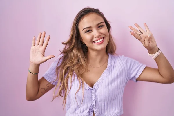 年轻的惊慌失措的女人站在粉红的背景上 用9号手指指指着 满面笑容 自信而快乐 — 图库照片