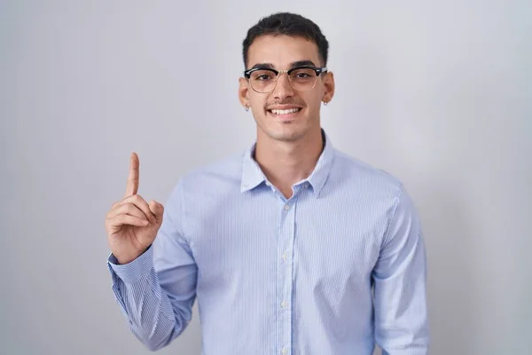 自信を持って幸せな笑顔でビジネス服や眼鏡を身に着けているハンサムなヒスパニック系の男と指の第1位を示すと指摘しながら — ストック写真