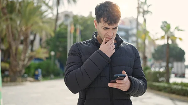 Joven Hombre Hispano Usando Teléfono Inteligente Mirando Molesto Parque —  Fotos de Stock