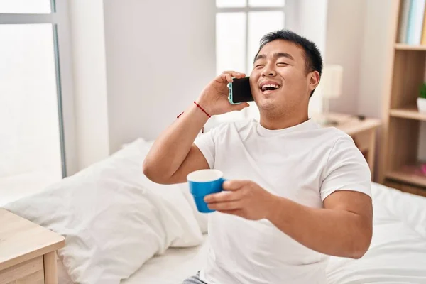Молодой Китаец Разговаривает Смартфону Пьет Кофе Сидя Кровати Спальне — стоковое фото