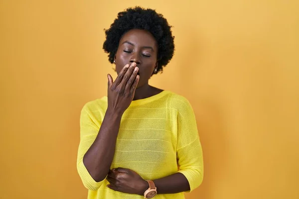 黄色のスタジオの上に立っているアフリカの若い女性は手で口をカバー疲れあくび退屈 落ち着きもなく眠気もなく — ストック写真