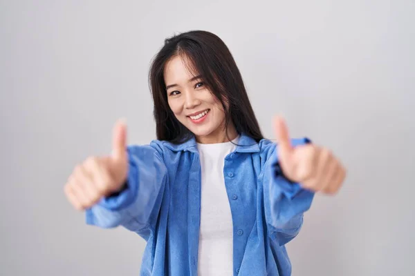 白い背景の上に立つ若い中国の女性は 手で積極的なジェスチャーを行うことを承認し 親指を笑顔と成功のために幸せ 勝者のジェスチャー — ストック写真