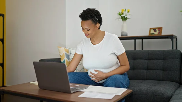 年轻的孕妇坐在沙发上在家做网上工作 — 图库照片