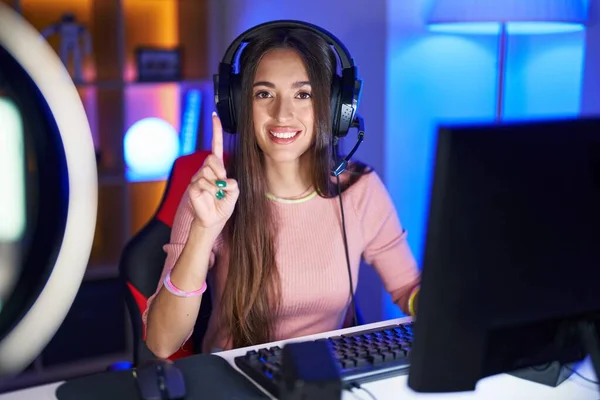 Stock image Young hispanic woman playing video games showing and pointing up with finger number one while smiling confident and happy. 