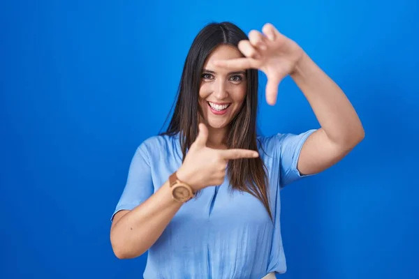 Young Brunette Woman Standing Blue Background Smiling Making Frame Hands — Stok fotoğraf