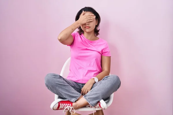 Латиноамериканская Молодая Женщина Сидящая Стуле Розовом Фоне Закрывая Глаза Рукой — стоковое фото