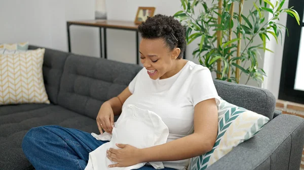 Jonge Zwangere Vrouw Met Babykleding Zittend Bank Thuis — Stockfoto