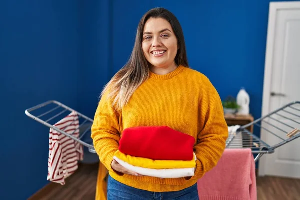 stock image Young hispanic woman holding clean and folded laundry smiling with a happy and cool smile on face. showing teeth. 