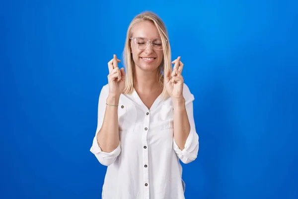 Young Caucasian Woman Standing Blue Background Gesturing Finger Crossed Smiling — Stockfoto