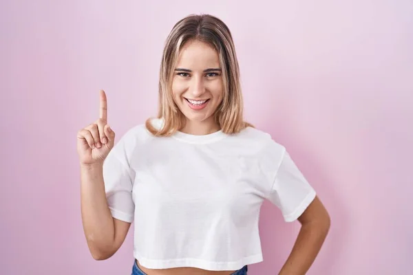 Young Blonde Woman Standing Pink Background Showing Pointing Finger Number — Foto de Stock
