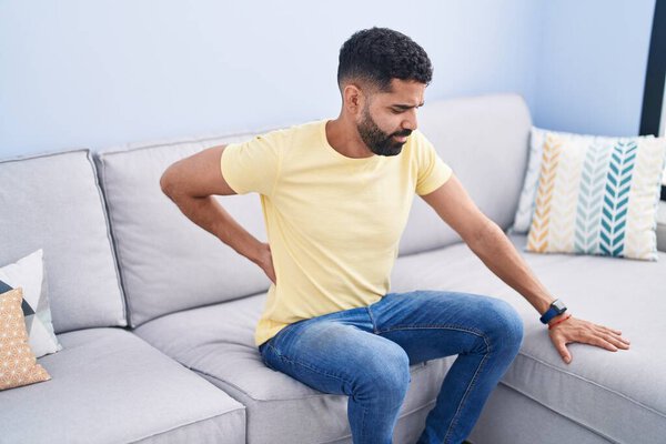 Молодой араб, страдающий от боли в спине, сидит дома на диване