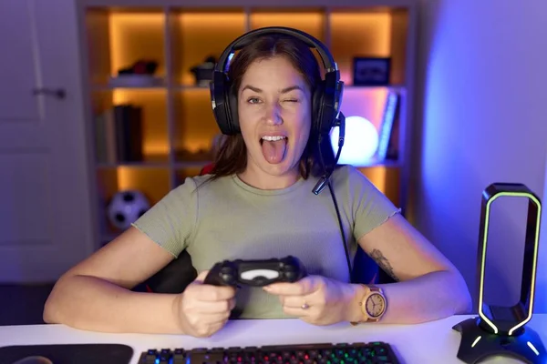 面白い表情で幸せな舌を突き出したヘッドフォンを身に着けているビデオゲームをしている美しいブルネットの女性 感情の概念 — ストック写真