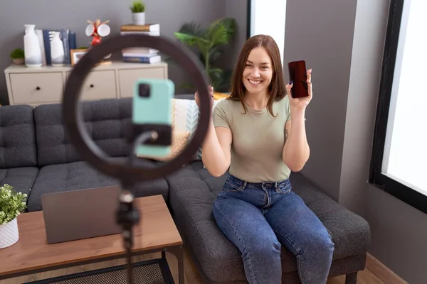 漂亮的黑发女人带着智能手机在家里录制Vlog教程 满面笑容 手指手画脚地指向旁边 — 图库照片