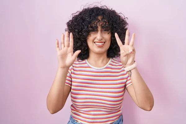 年轻的中东女人站在粉红的背景上 用八号手指指指着 自信而快乐地微笑着 — 图库照片