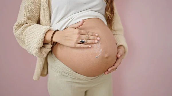Молодая Беременная Женщина Массирует Живот Лосьоном Ухода Кожей Изолированном Розовом — стоковое фото