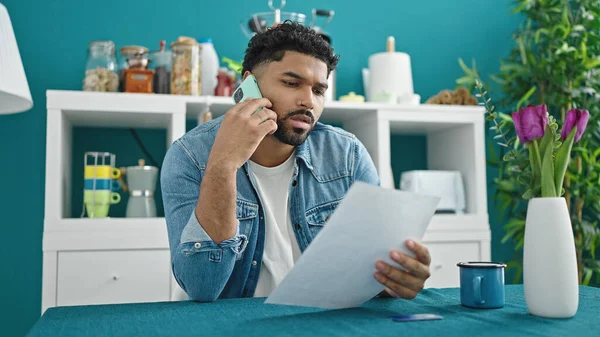 Stock image African american man talking on smartphone reading document at dinning room