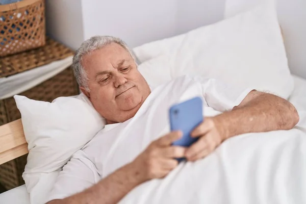 寝室のベッドに横たわっスマートフォンを使用して中世の白髪の男 — ストック写真