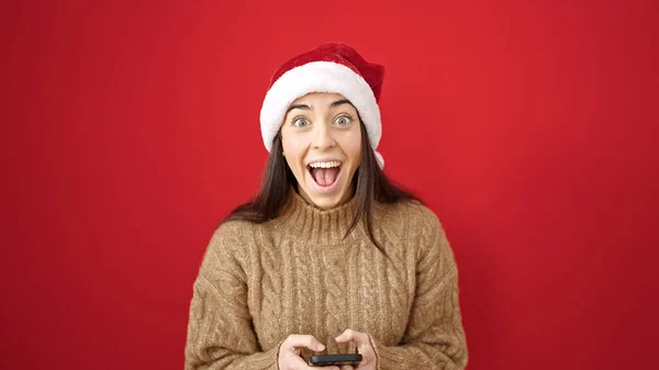 Junge Schöne Hispanische Frau Trägt Weihnachtsmütze Mit Smartphone Mit Überraschungsausdruck — Stockfoto