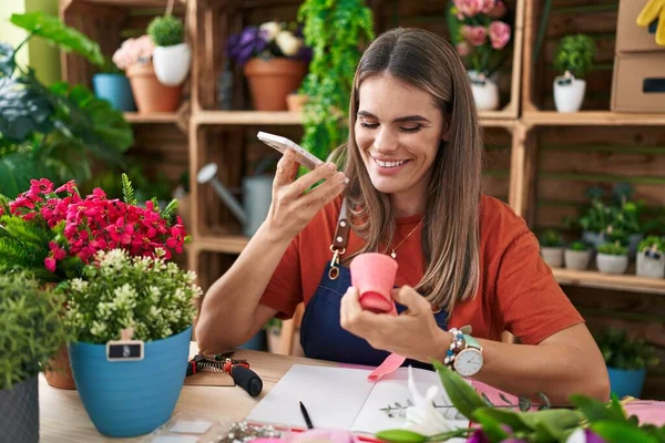 年轻美丽的惊慌失措的女花匠拿着礼物花边在花店里用智能手机说话 — 图库照片