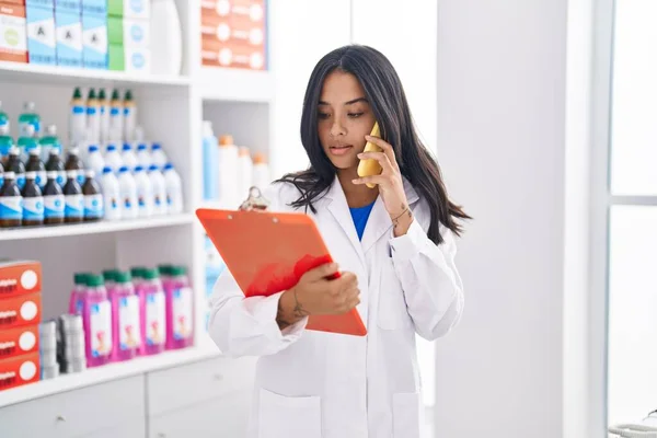 Young Hispanic Woman Pharmacist Talking Smartphone Reading Document Pharmacy — 스톡 사진