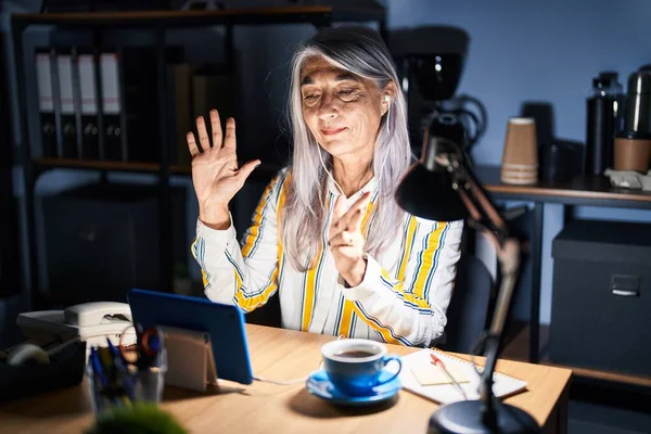 白发苍苍的中年妇女晚上在办公室里工作时 露出八号手指指尖 面带微笑 自信而快乐 — 图库照片