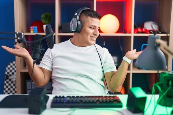 若いヒスパニック系の男は両手を開いてヤシの木を示す笑みを浮かべてビデオゲームをプレイ プレゼンテーションと広告の比較とバランス — ストック写真