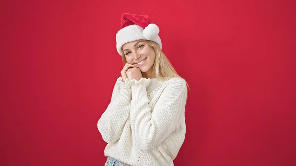 Молода Блондинка Посміхається Впевнено Носить Різдвяний Капелюх Над Ізольованим Червоним — стокове фото