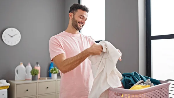 年轻的惊慌失措的男人带着自信的笑容在洗衣房闻干净的毛巾 — 图库照片