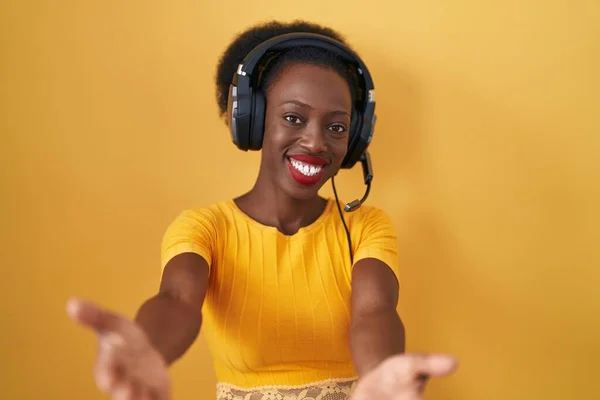 Африканская Женщина Вьющимися Волосами Стоит Жёлтом Фоне Наушниках Смотрит Камеру — стоковое фото