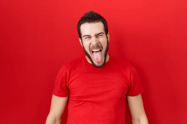 年轻的他的惊慌失措的男人穿着休闲的红色T恤 带着滑稽的表情伸出舌头 很高兴 情感概念 — 图库照片