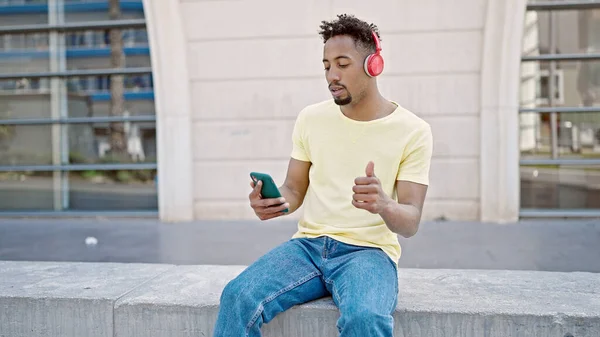 アフリカ系アメリカ人の男性が路上で親指を立ててスマートフォンを使って音楽を聴く — ストック写真