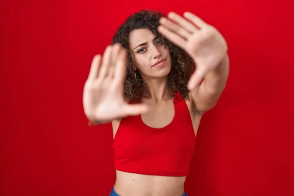 Kıvırcık Saçlı Spanyol Kadın Kırmızı Arka Planda Duruyor Parmaklarıyla Çerçeve — Stok fotoğraf