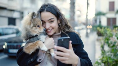 Köpeğiyle gülümseyen genç İspanyol kadın. Sokakta akıllı telefon kullanıyor.