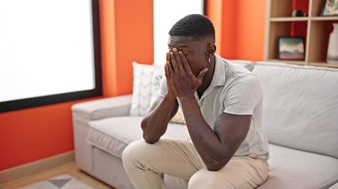 Afrikalı Amerikalı adam evdeki kanepede otururken stresli.