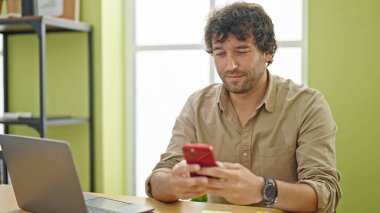 Young hispanic man business worker using smartphone at office