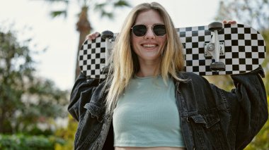 Parkta patenle kayarken gülümseyen genç sarışın kadın.