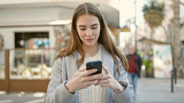 Kahve dükkanının terasında akıllı telefon kullanan genç İspanyol kadın.