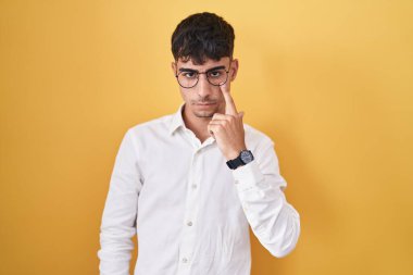 Sarı arka planda dikilen İspanyol genç adam senin jestini ve şüpheli ifadesini izleyerek göze işaret ediyor. 