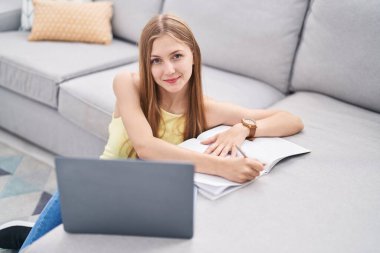 Evde dizüstü bilgisayar kullanan beyaz bir kadın var.