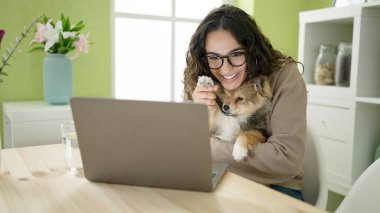 Köpekli genç İspanyol kadın yemek odasında video görüşmesi yapıyor.