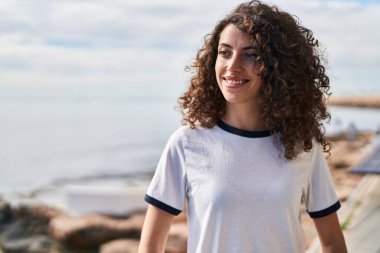 Young hispanic woman smiling confident looking to the side at seaside